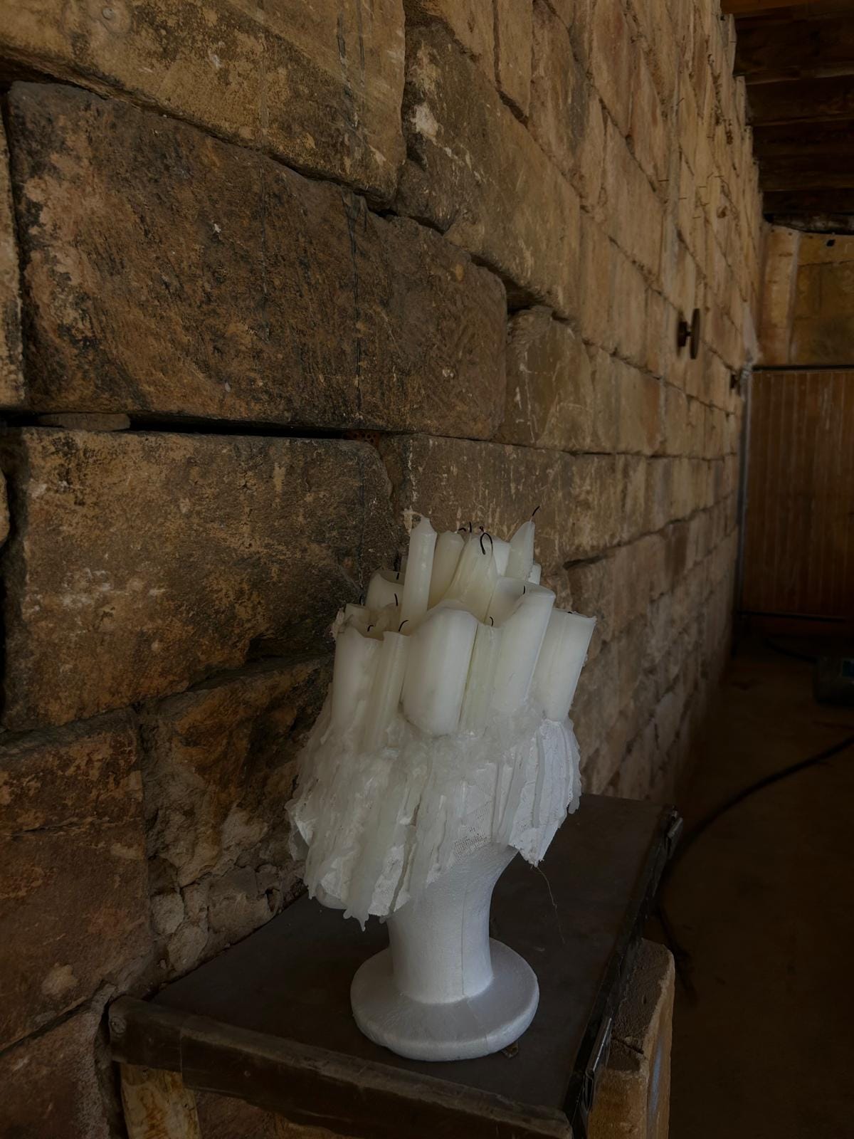 Tocado de velas terminado sobre peana junto a un muro de piedra