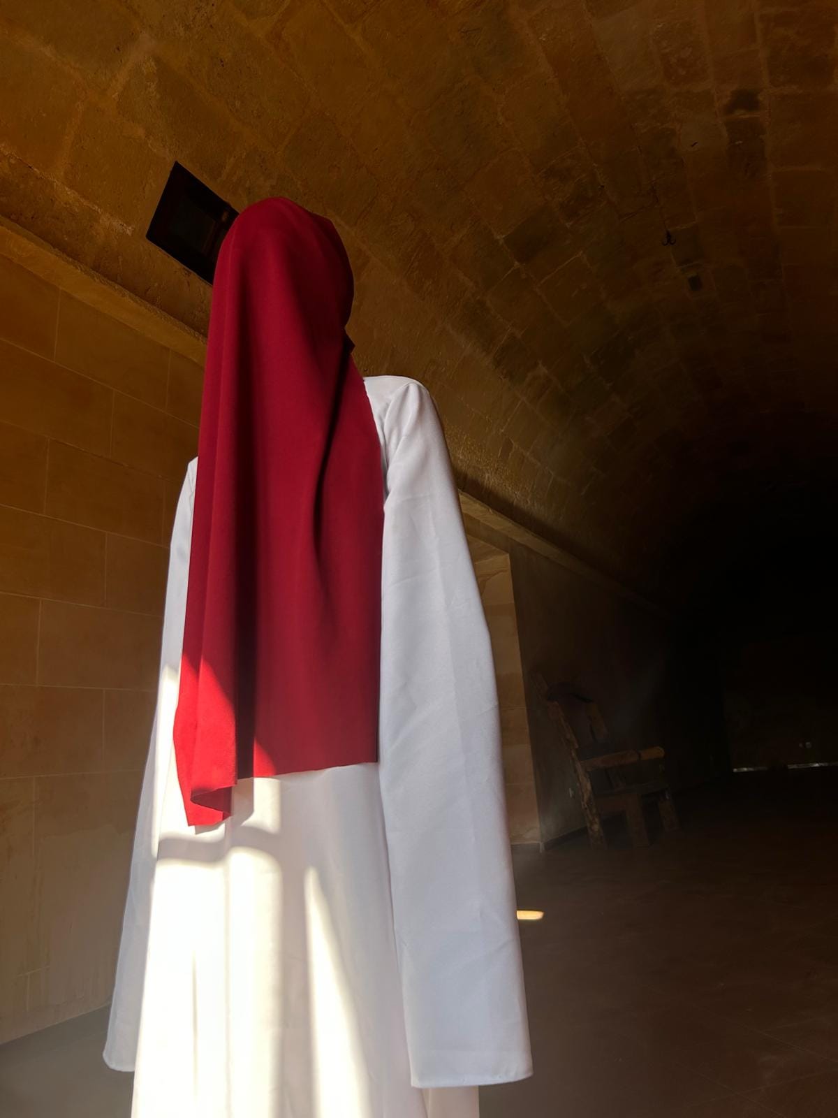 Figura con tela roja sobre la cabeza y túnica blanca en una bóveda de piedra
